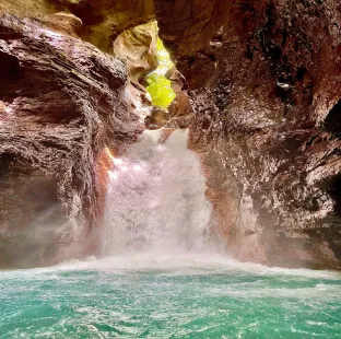 A waterfall cascades between dark rock walls into a pool of bright turquoise water.