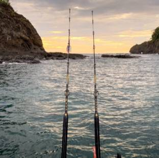 Two fishing rods are positioned over water, facing a rocky shoreline at sunset.
