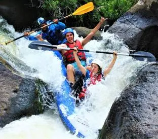 Three people wearing helmets and life jackets navigate a blue kayak through rocky rapids.