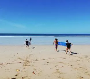People walking along the beach towards the sea carrying surfboards under a clear sky.