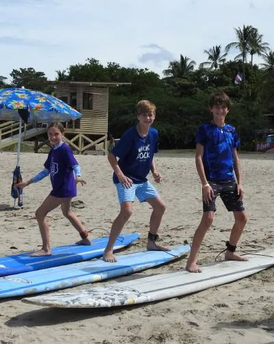 Three young people practice balancing on surfboards on a beach with a lifeguard tower.