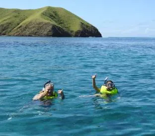 Two people with snorkeling gear and yellow life jackets swim in tropical blue waters.