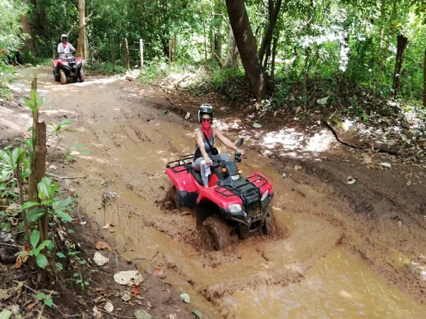 A person wearing a helmet drives a red all-terrain vehicle through a muddy road.