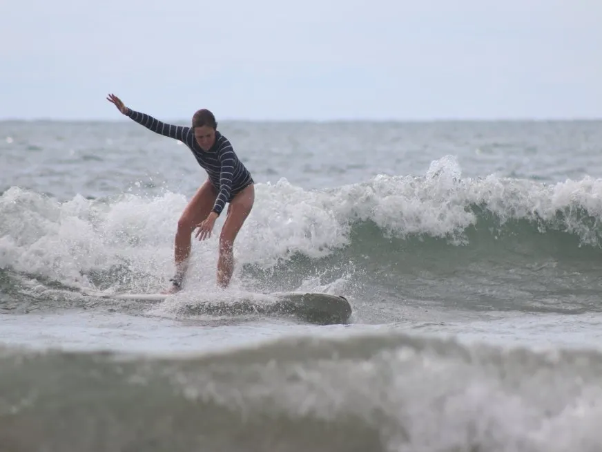A woman in a striped swimsuit surfs on a wave in the sea.