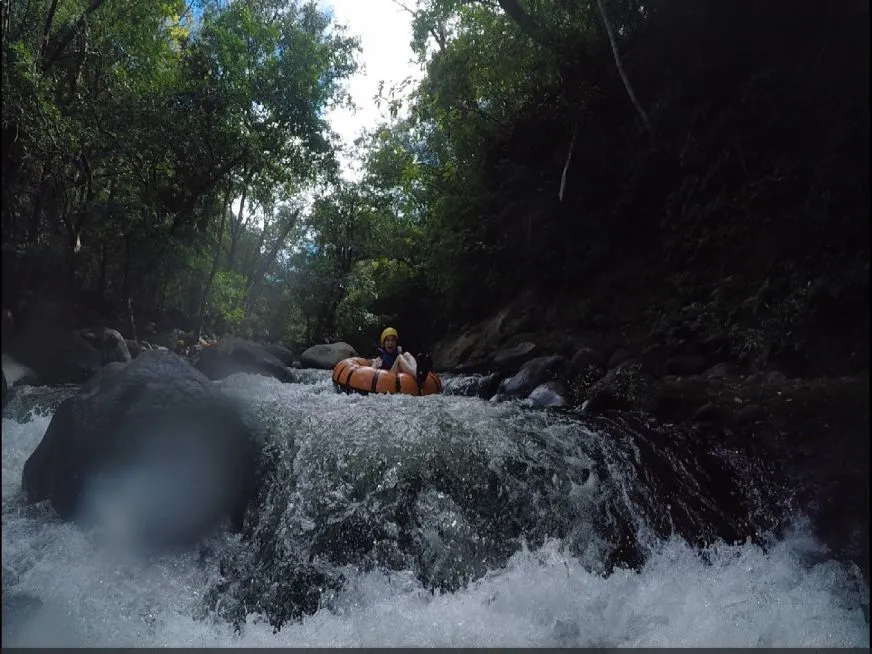 A person wearing a yellow helmet descends a fast-flowing river on an orange inflatable float.