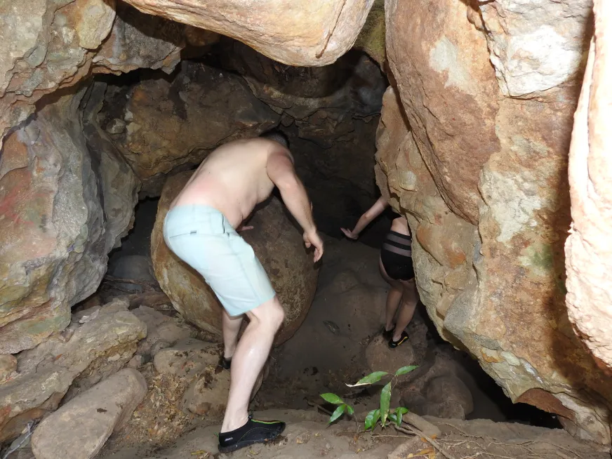 A man and a woman explore a cave with natural rock formations and uneven ground.