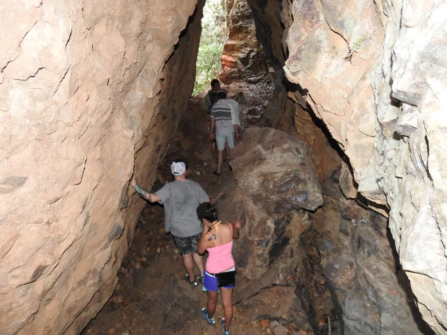 A group of people walks through a narrow passage between large rock formations.