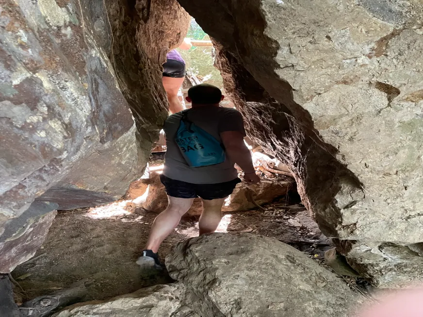 A man with a blue waterproof backpack walks through a narrow passage between rocks.