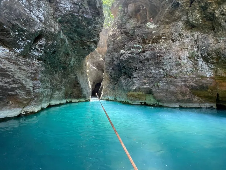 A rope crosses a turquoise river between two large, craggy rock walls.