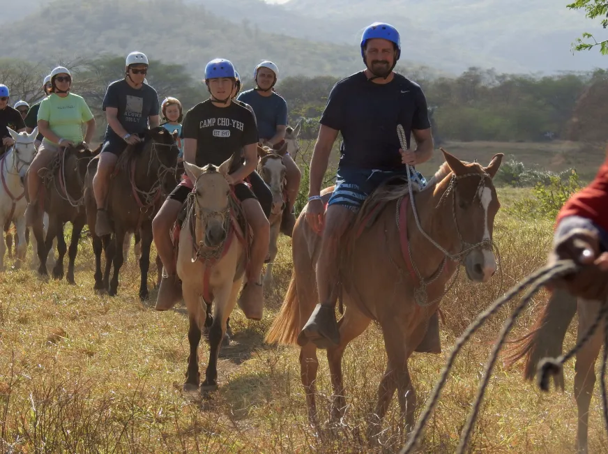 A group of tourists ride horses together along a open dirt trail in the countryside.