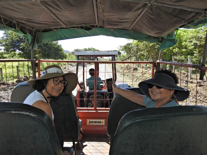 Tourists sit inside a covered vehicle during a guided tour through a tropical landscape.