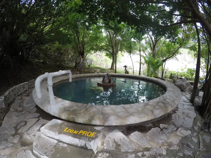 A circular stone thermal pool surrounded by lush green tropical garden and trees.