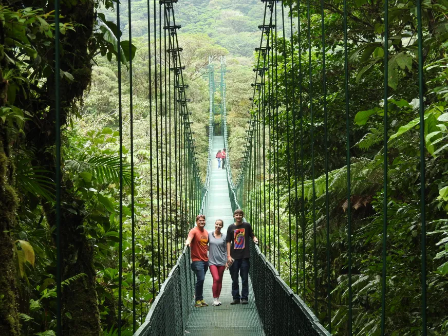 Three people pose on a suspension bridge surrounded by the dense vegetation of a tropical forest.