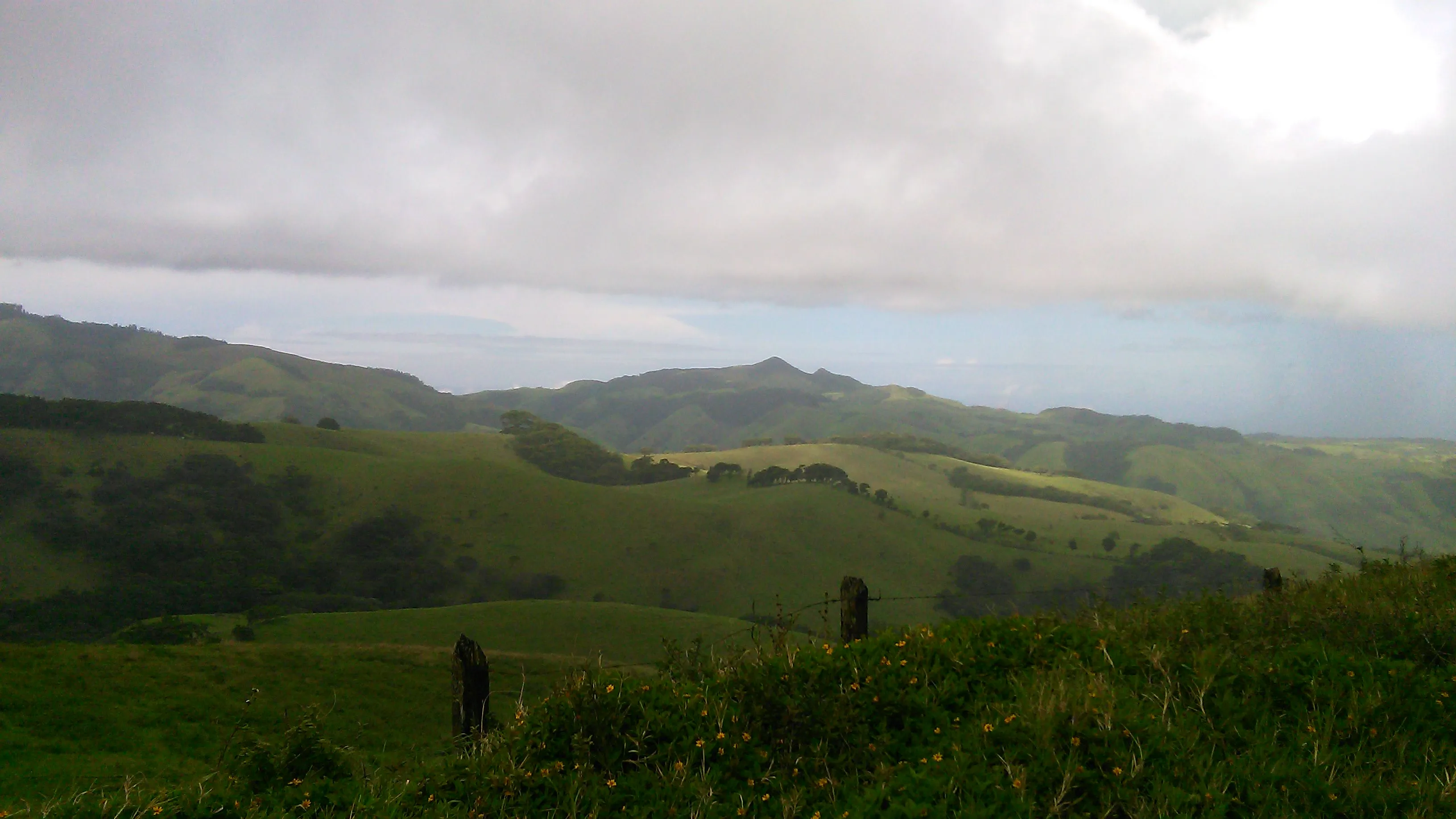 Rolling green hills under a cloudy sky with a wooden fence in the foreground.