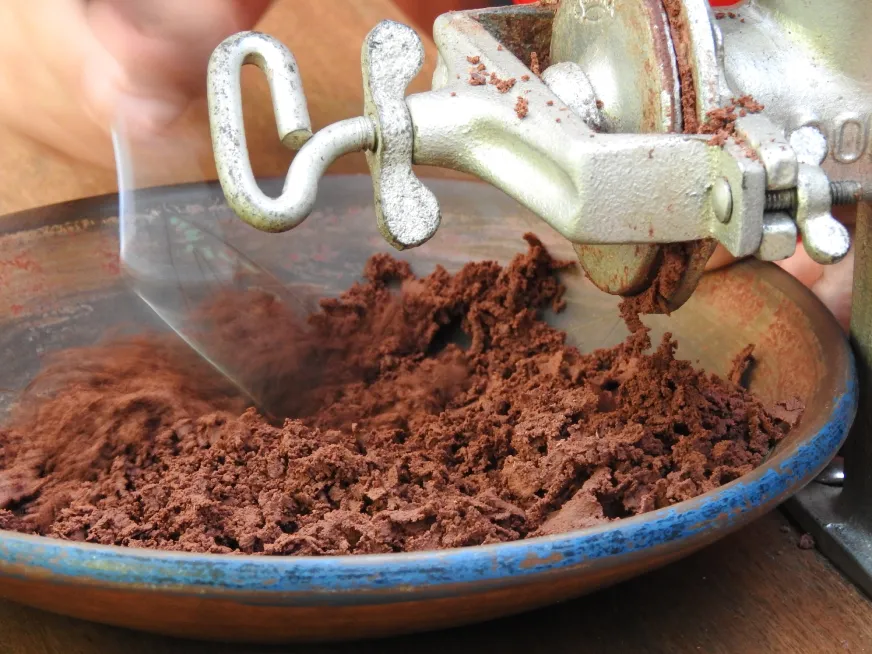 A metal mill grinds cocoa powder over a blue-rimmed ceramic bowl.
