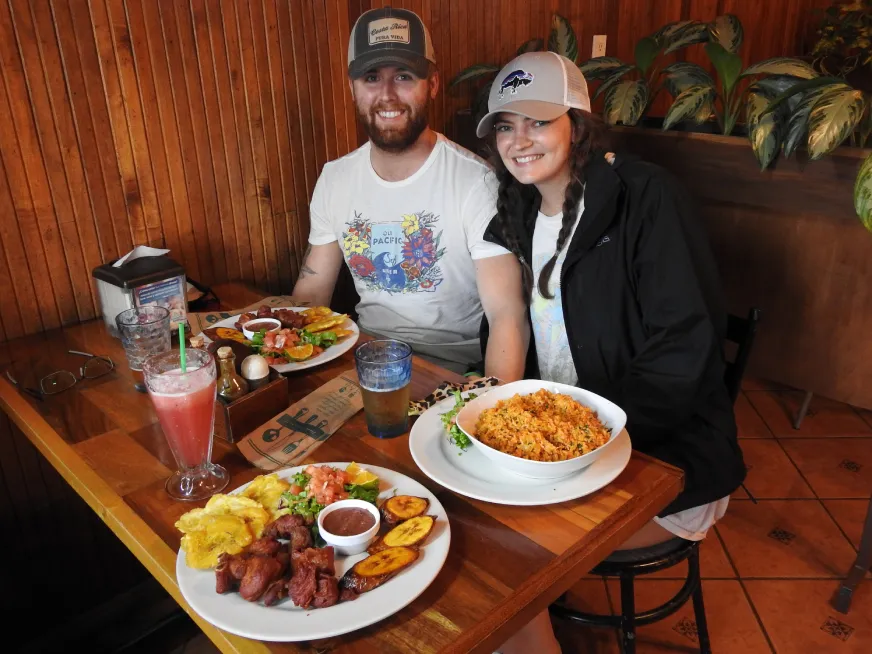 A smiling couple sitting at a restaurant table with typical food dishes and drinks.