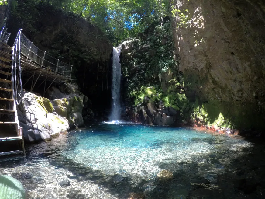 A waterfall cascades into a vivid turquoise pool inside a narrow rocky canyon.