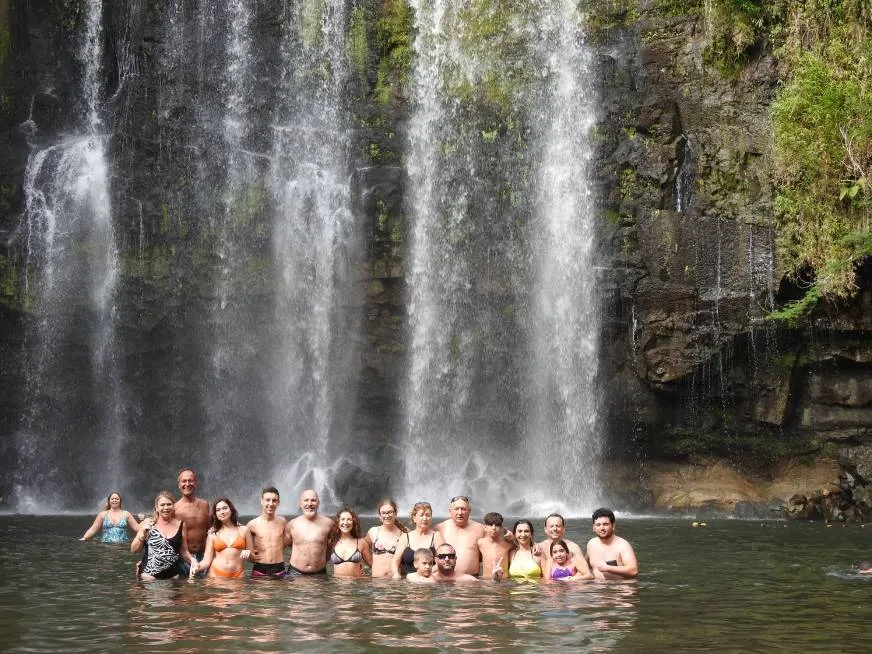 A group of tourists swim and enjoy a natural pool at the base of a tall waterfall.