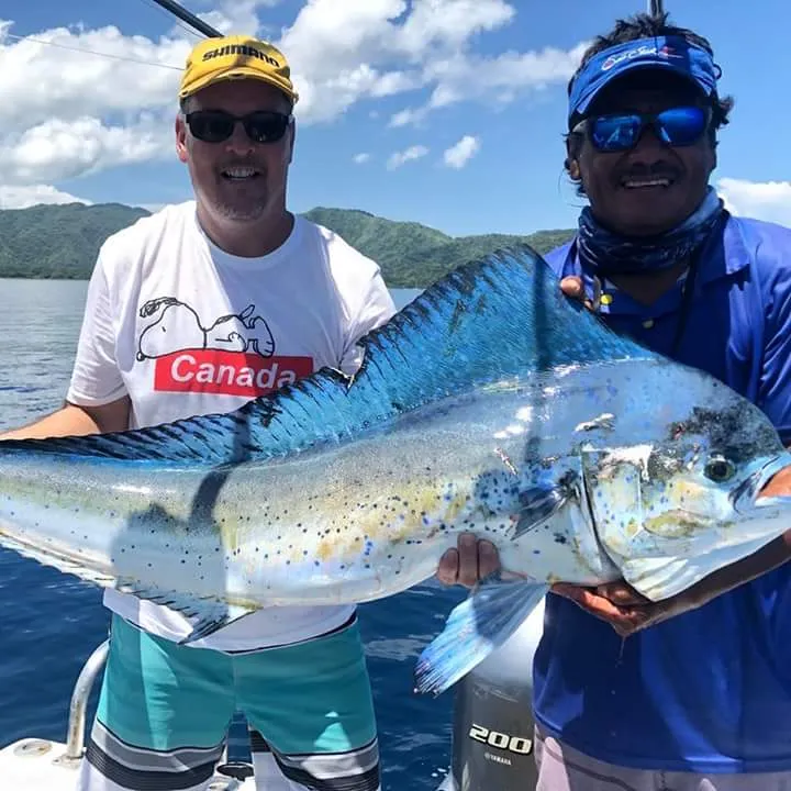 Two smiling men hold a large goldfish on a boat in the open sea.