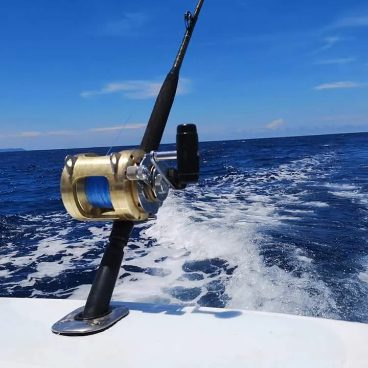 Fishing rod with golden reel mounted on a boat over the deep blue sea.