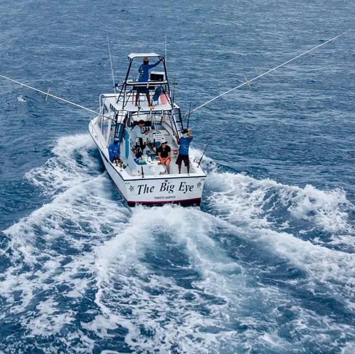 A fishing boat called The Big Eye sailing on blue waters with several people on board.