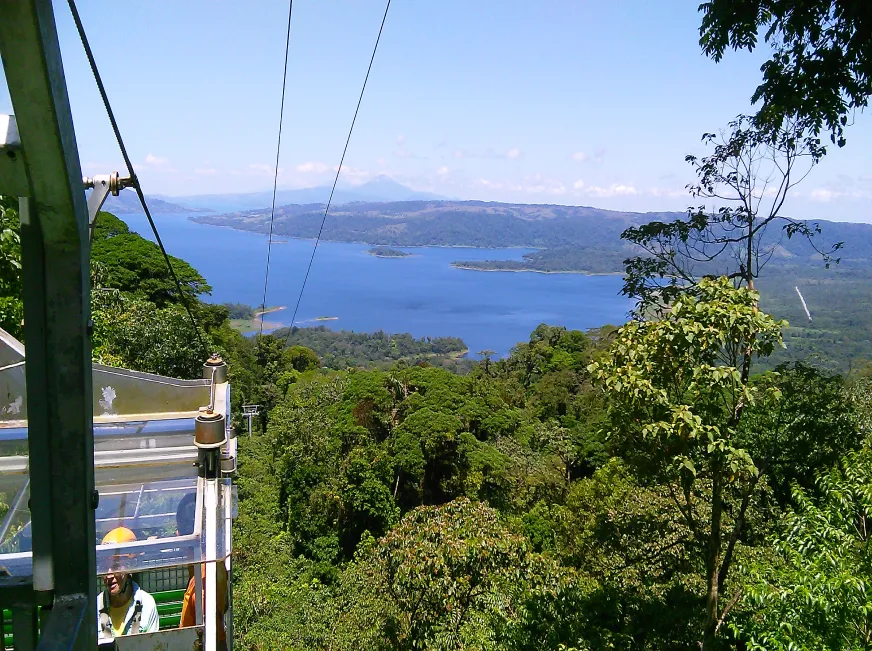 A zip line cable stretches above a scenic blue lake surrounded by green hills and clear sky.